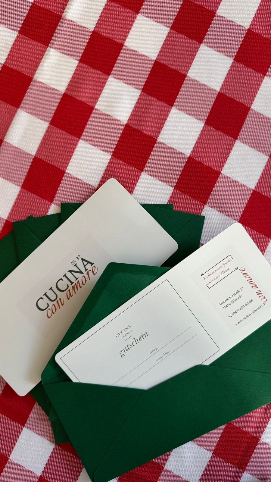 Gutschein von Cucina con amore im grünen Umschlag auf karierter Tischdecke