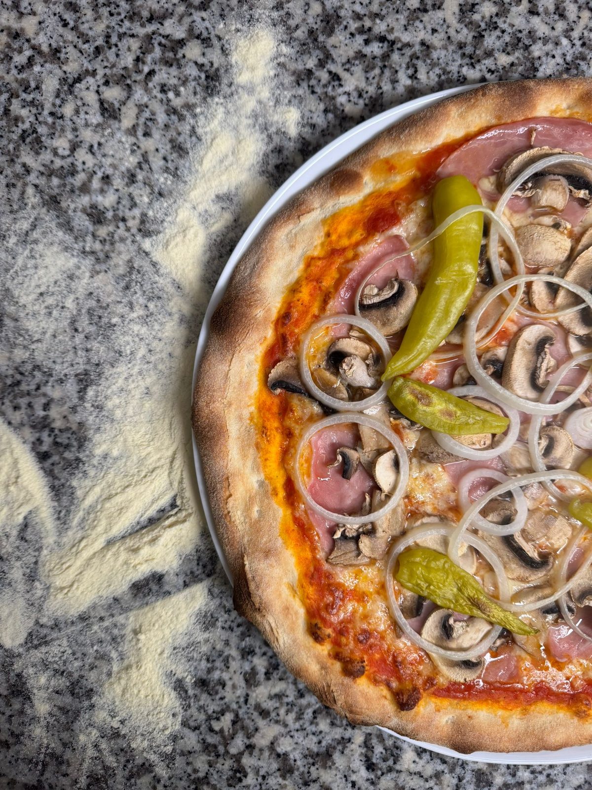 Pizza mit Schinken, Champignons, Zwiebeln und Peperoni auf bemehltem Stein